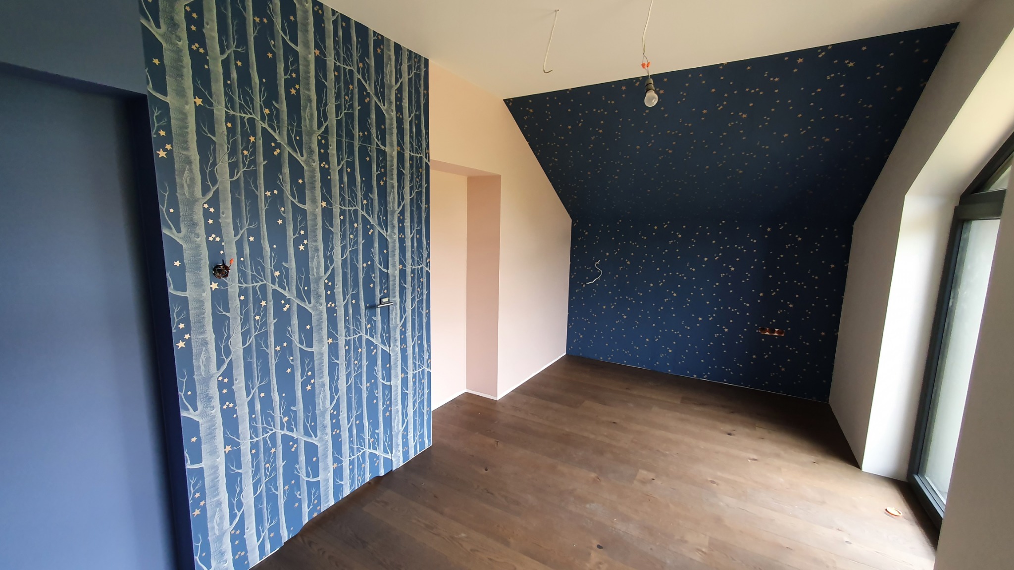 Pokój po remoncie z nową tapetą: na jednej ścianie granatowa tapeta w białe drzewa z gwiazdkami, na drugiej granatowa tapeta w złote gwiazdki, drewniana podłoga.