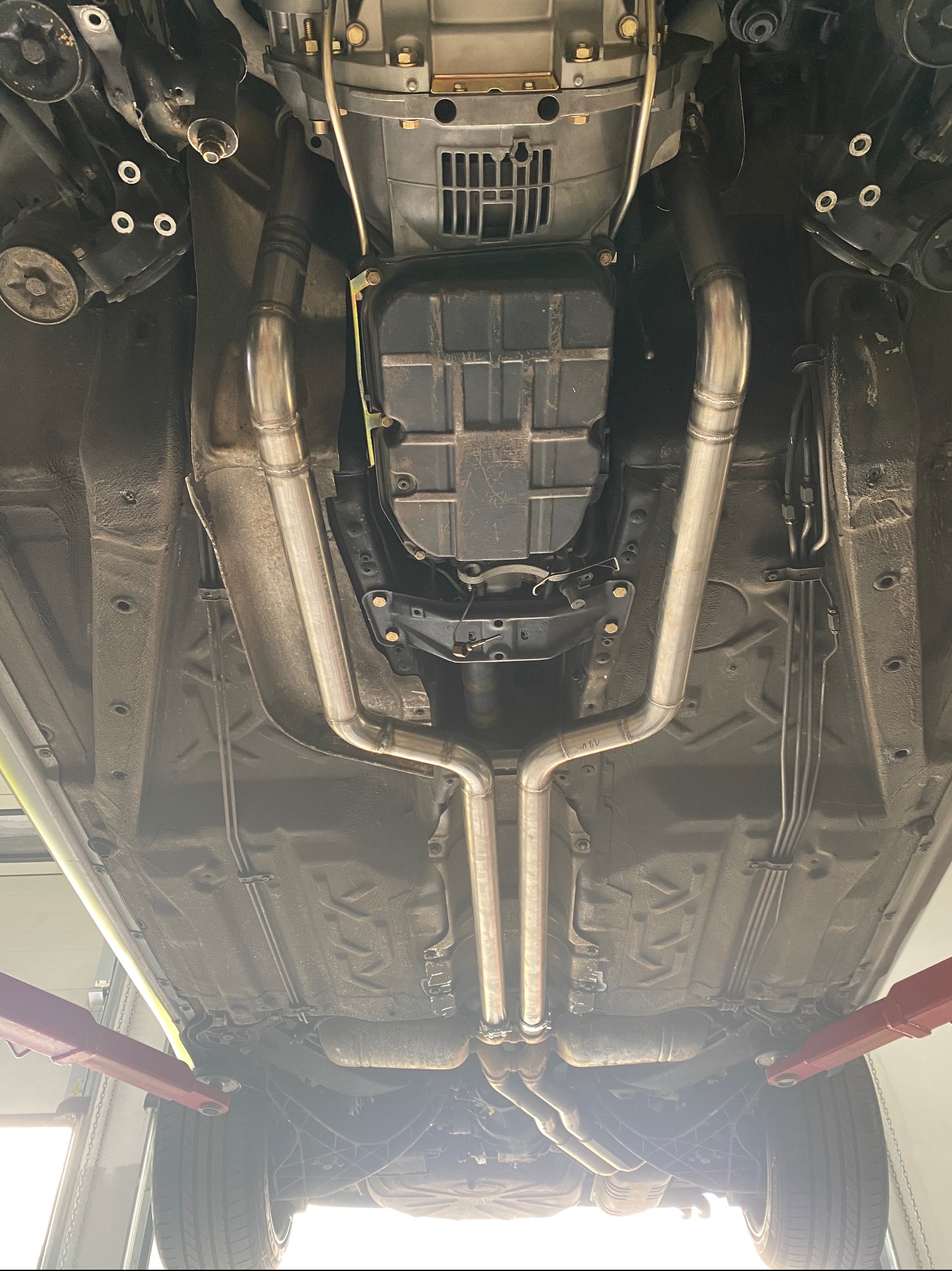 Widok podwozia samochodu na podnośniku z nowym, nierdzewnym układem wydechowym, widoczne spawane łączenia rur.