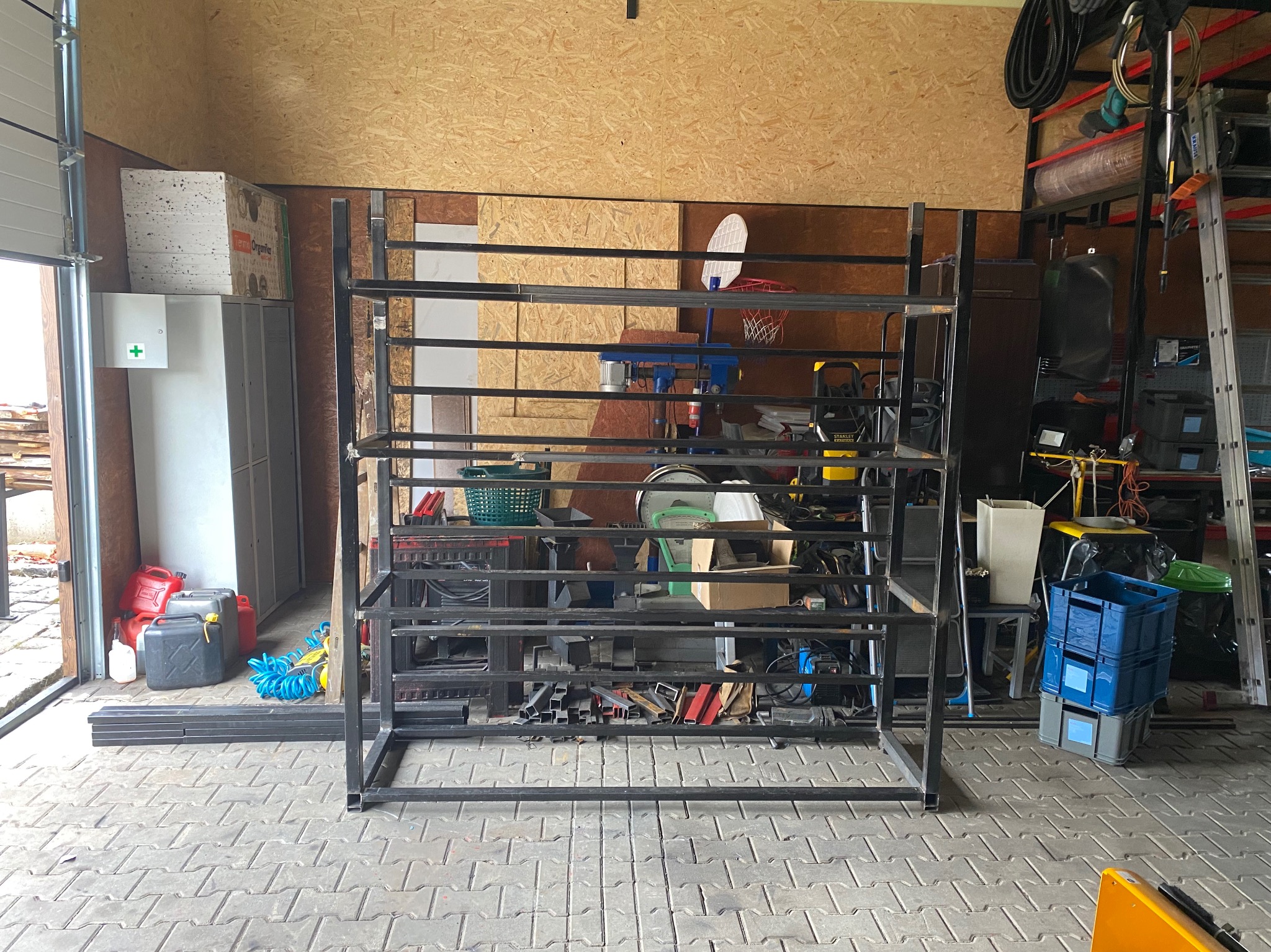 Metalowa konstrukcja regału z profili w warsztacie, widoczne narzędzia, skrzynki i inne elementy wyposażenia.
