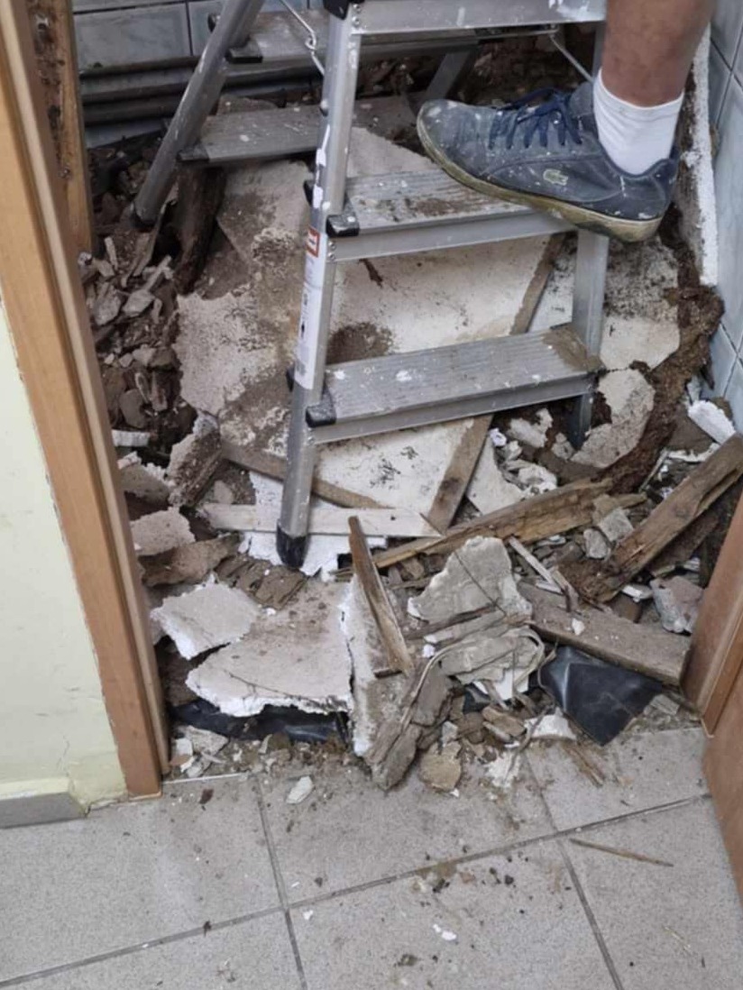 Demontaż podłogi w łazience: widoczne gruz, fragmenty płytek, drewniane elementy i drabina z butem na jednym ze stopni, przygotowanie do remontu.