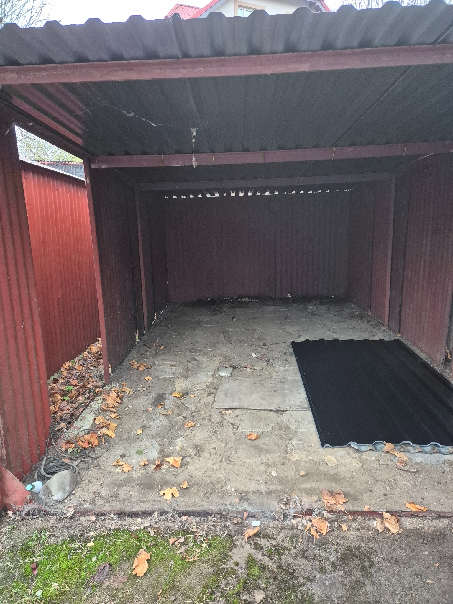 Otwarta wiata z blachy trapezowej, widoczne liście na podłodze i zwinięty kabel w rogu, przygotowana do remontu lub sprzątania.