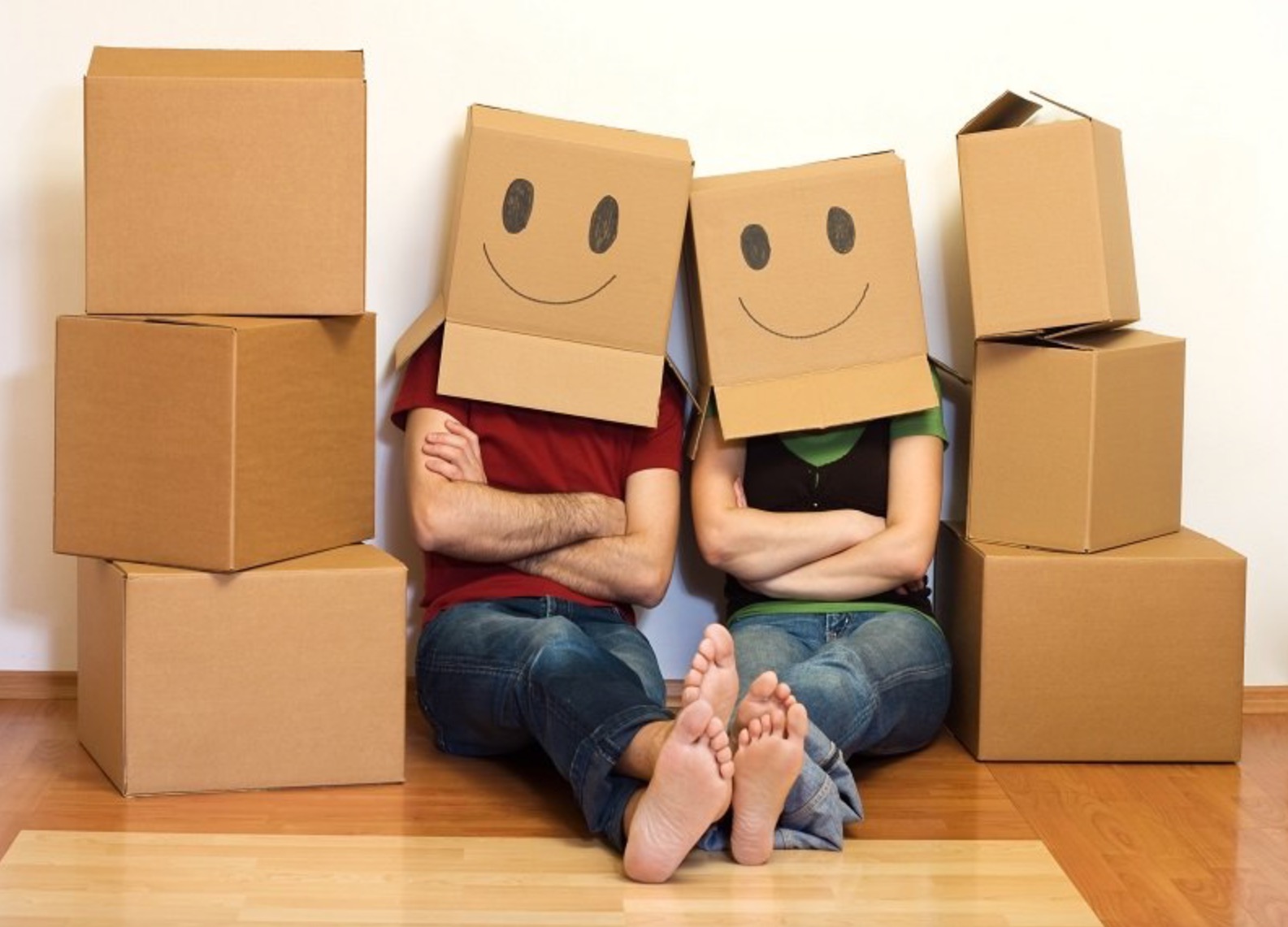 Para siedzi na podłodze z pudełkami z narysowanymi uśmiechami na głowach, stopy skierowane do przodu.