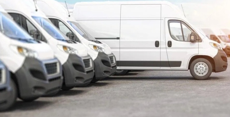 Rząd białych samochodów dostawczych zaparkowanych obok siebie, widok z niskiego kąta, z lekkim efektem rozmycia w tle.