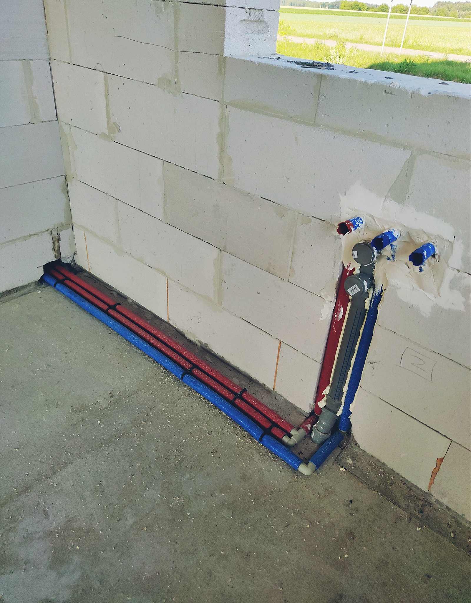 Wewnętrzne ściany z betonu komórkowego z instalacją wodną i ogrzewania podłogowego w trakcie montażu. Rury w izolacji czerwonej i niebieskiej prowadzone wzdłuż ściany, pionowe rury w piankowej...