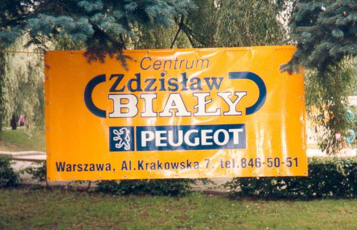 Żółty baner reklamowy z niebieskim logo Peugeot i napisem 'Centrum Zdzisław Biały' na tle zieleni.