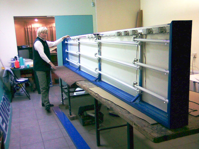 Montaż wewnętrznego oświetlenia w kasetonie reklamowym przez pracownika w warsztacie, widoczne świetlówki, elementy mocujące i rama kasetonu.