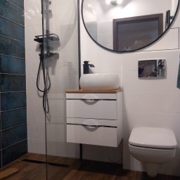 Dmytro Marynchenko - Nowoczesna łazienka z kabiną prysznicową typu walk-in, umywalką nablatową na szafce z dwiema szufladami, okrągłym lustrem w czarnej ramie i podwieszaną toaletą.