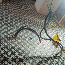 Dmytro Marynchenko - Układanie płytek podłogowych w łazience z wzorem geometrycznym gwiazd, widoczne kable elektryczne i lampa robocza.