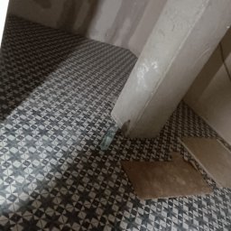 Dmytro Marynchenko - Układanie wzorzystych płytek podłogowych w surowym wnętrzu łazienki, widoczne niedokończone ściany i narzędzia glazurnicze.