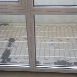 Dmytro Marynchenko - Instalacja ogrzewania podłogowego elektrycznego w trakcie zalewania wylewką, widoczne kable grzewcze i fragment okna.