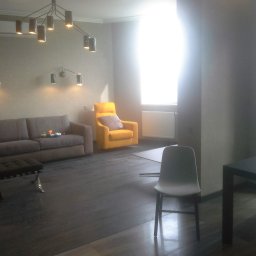 Dmytro Marynchenko - Salon z szarą sofą, żółtym fotelem i ciemną drewnianą podłogą, oświetlony nowoczesnymi lampami sufitowymi i ściennymi.