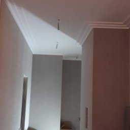 Dmytro Marynchenko - Korytarz w trakcie remontu, widoczne szpachlowane ściany, listwy sufitowe i kable zwisające z sufitu, podłoga zabezpieczona folią malarską.
