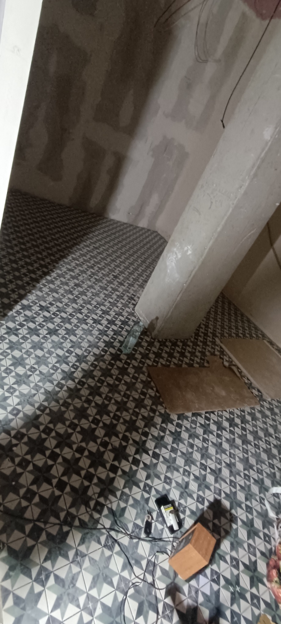 Układanie wzorzystych płytek podłogowych w surowym wnętrzu łazienki, widoczne niedokończone ściany i narzędzia glazurnicze.