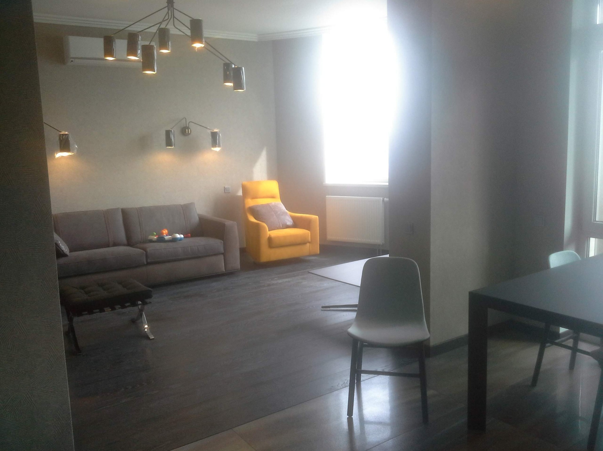 Salon z szarą sofą, żółtym fotelem i ciemną drewnianą podłogą, oświetlony nowoczesnymi lampami sufitowymi i ściennymi.