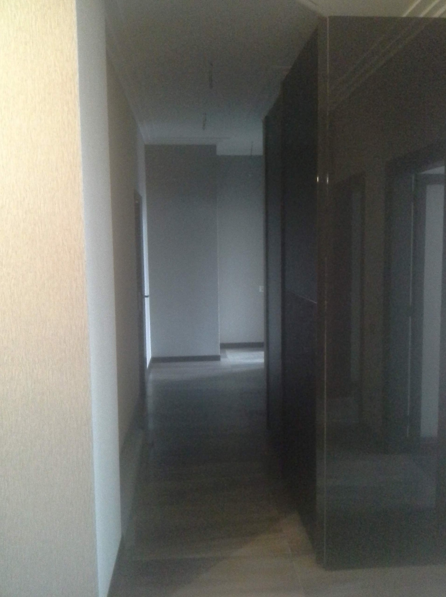 Wnętrze korytarza po remoncie z szarą podłogą i jasnymi ścianami, widoczne drzwi w głębi.