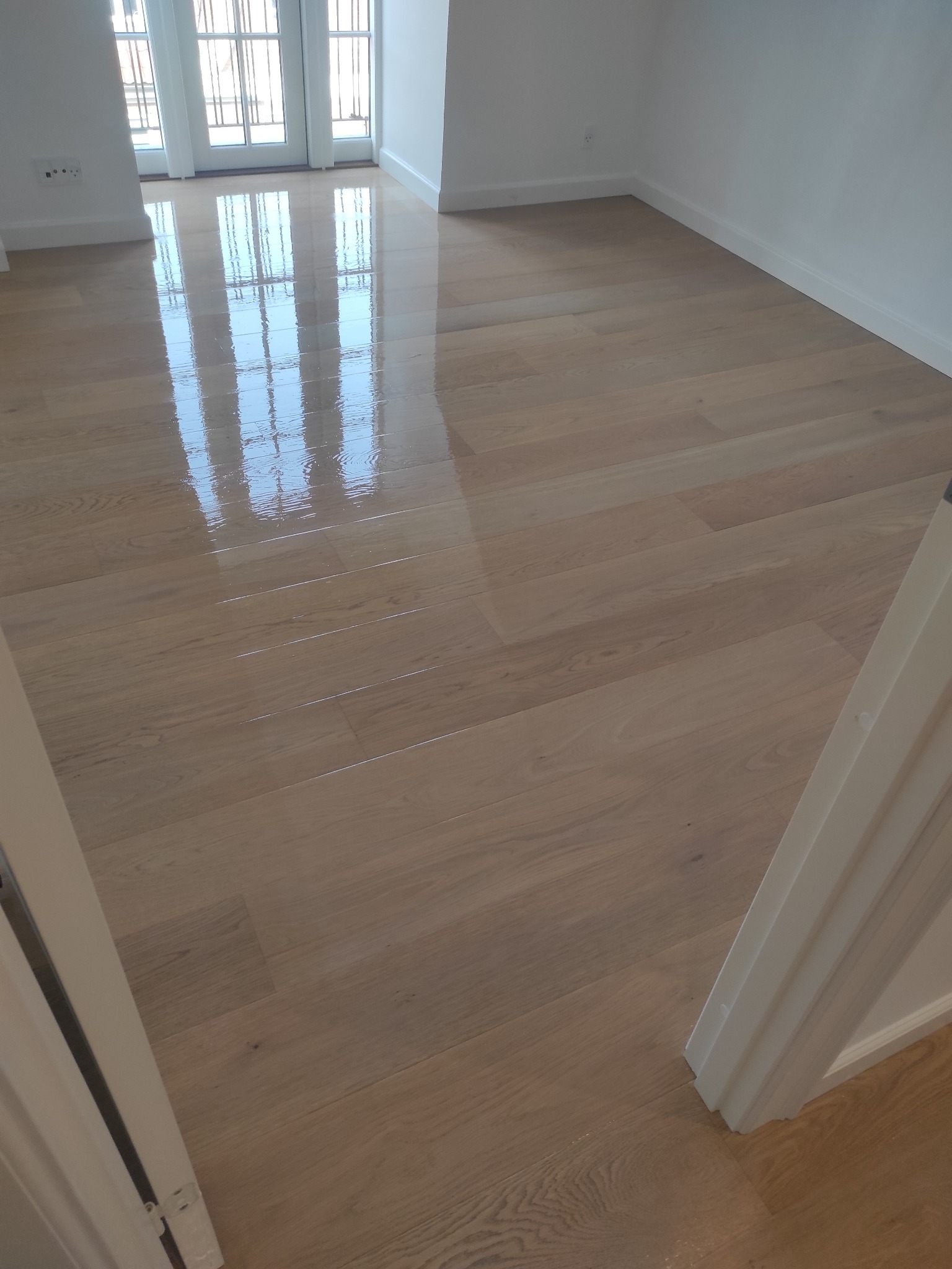 Świeżo wycyklinowana, lakierowana podłoga parkietowa z wyraźnym odbiciem okien balkonowych, widoczna listwa przypodłogowa.