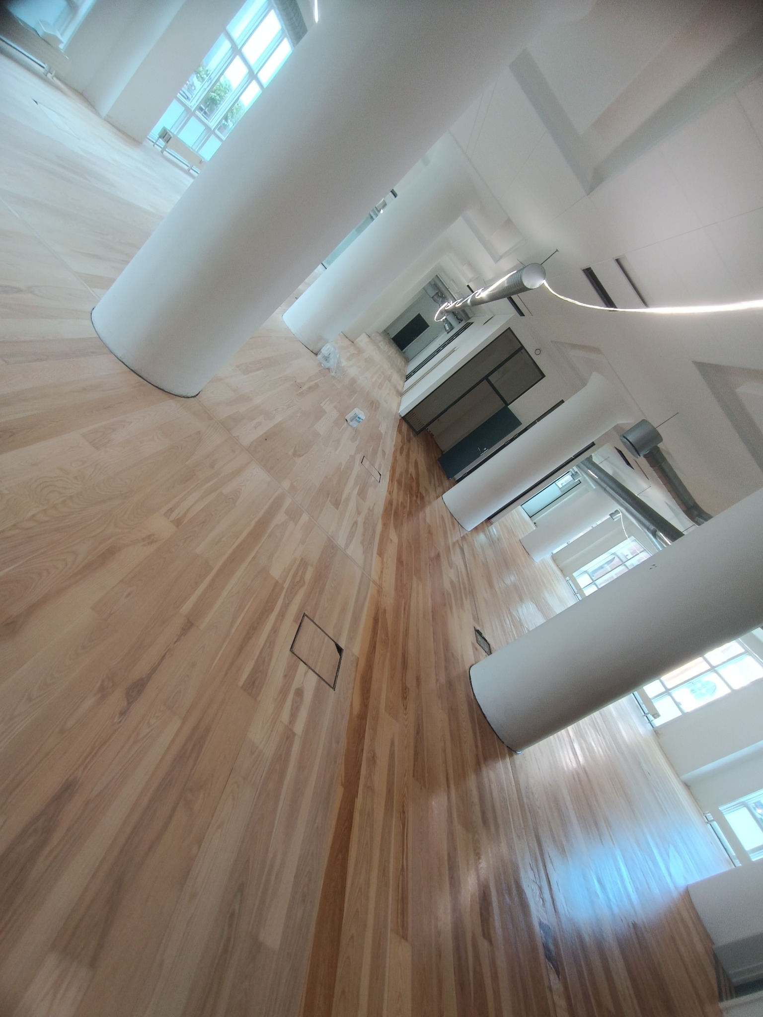 Jasny, drewniany parkiet ułożony w dużym pomieszczeniu z białymi kolumnami i oknami w tle, widok z dołu w kierunku sufitu.