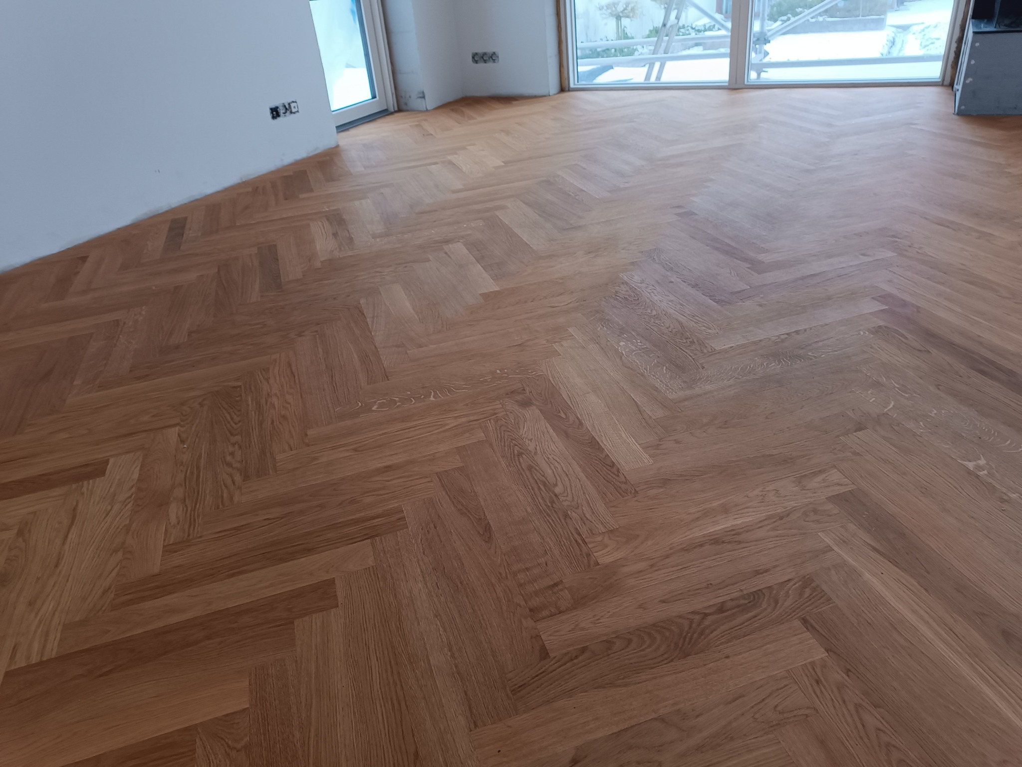 Ułożony parkiet w jodełkę francuską, widoczne okna z widokiem na zewnątrz, ściany przygotowane do malowania.