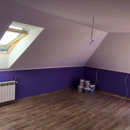 EcoClin - Pomalowane na fioletowo poddasze z oknem dachowym, grzejnikiem i panelami podłogowymi. Widoczne puszki z farbą i wystające kable elektryczne.