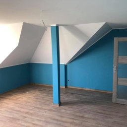 EcoClin - Pomalowane na biało i turkusowo poddasze ze skosami, drewnopodobna podłoga i drzwi z przeszkleniami. Kolumna w kolorze ścian. Widok na wykończone wnętrze.