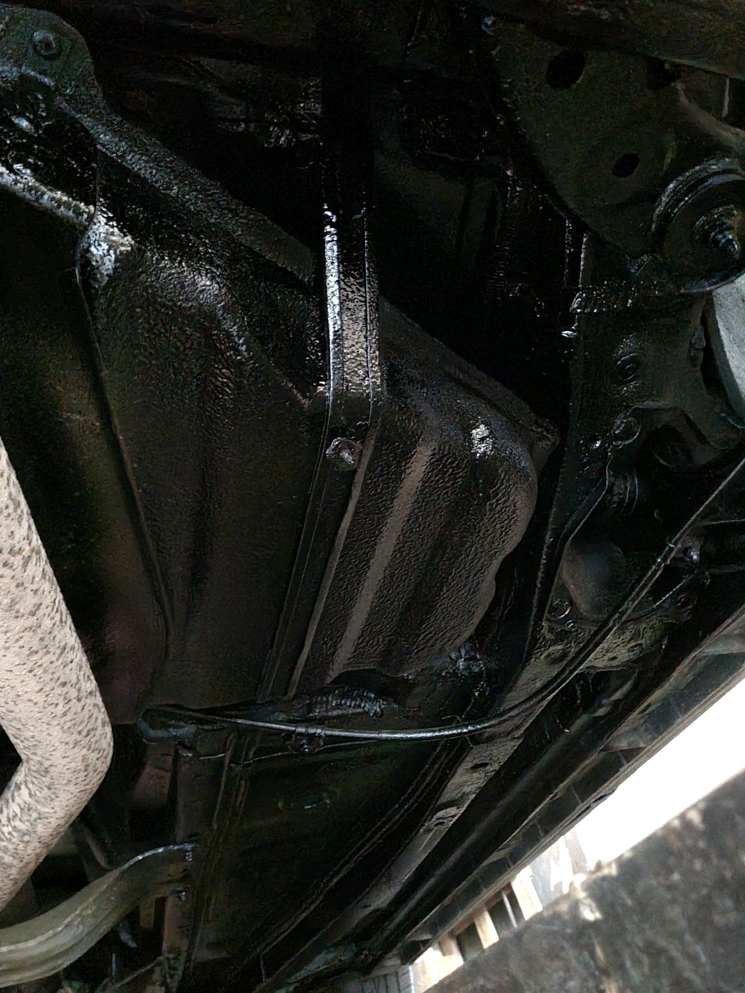 Podwozie samochodu po nałożeniu grubej, czarnej warstwy ochronnej; widoczny układ wydechowy z bliska.