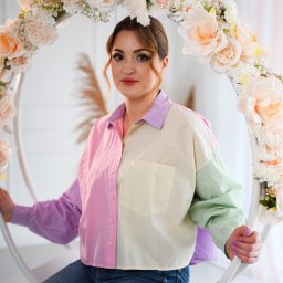 FotoArtNyk - Kobieta siedzi na białej huśtawce udekorowanej kremowymi różami, ubrana w jeansy i koszulę w pastelowych kolorach.