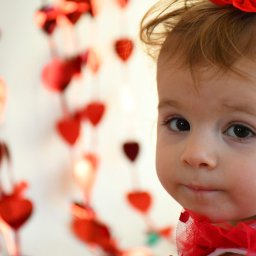 FotoArtNyk - Portret dziewczynki z czerwoną kokardą we włosach i naszyjnikiem z czerwonej siateczki, w tle girlanda z czerwonych serc.