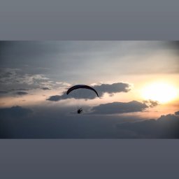 FotoArtNyk - Paralotniarz z silnikiem wznosi się na tle zachodzącego słońca i chmur.