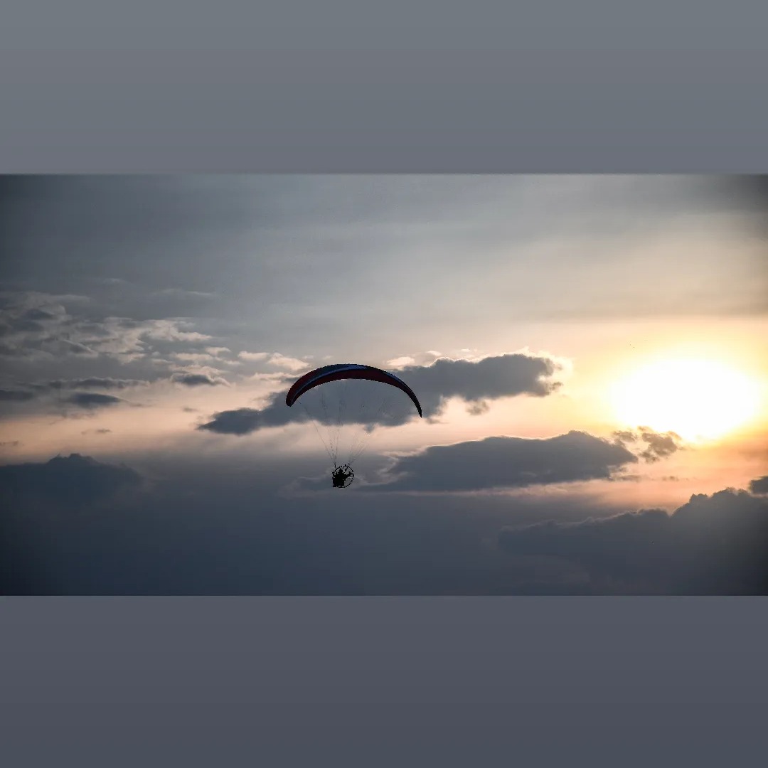 Paralotniarz z silnikiem wznosi się na tle zachodzącego słońca i chmur.