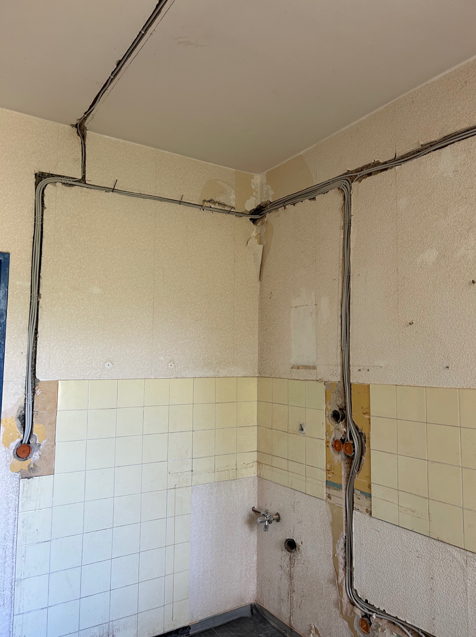 Szare kable elektryczne ułożone w bruzdach na ścianach i suficie kuchni w trakcie remontu. Widoczne puszki instalacyjne i fragmenty starej glazury.