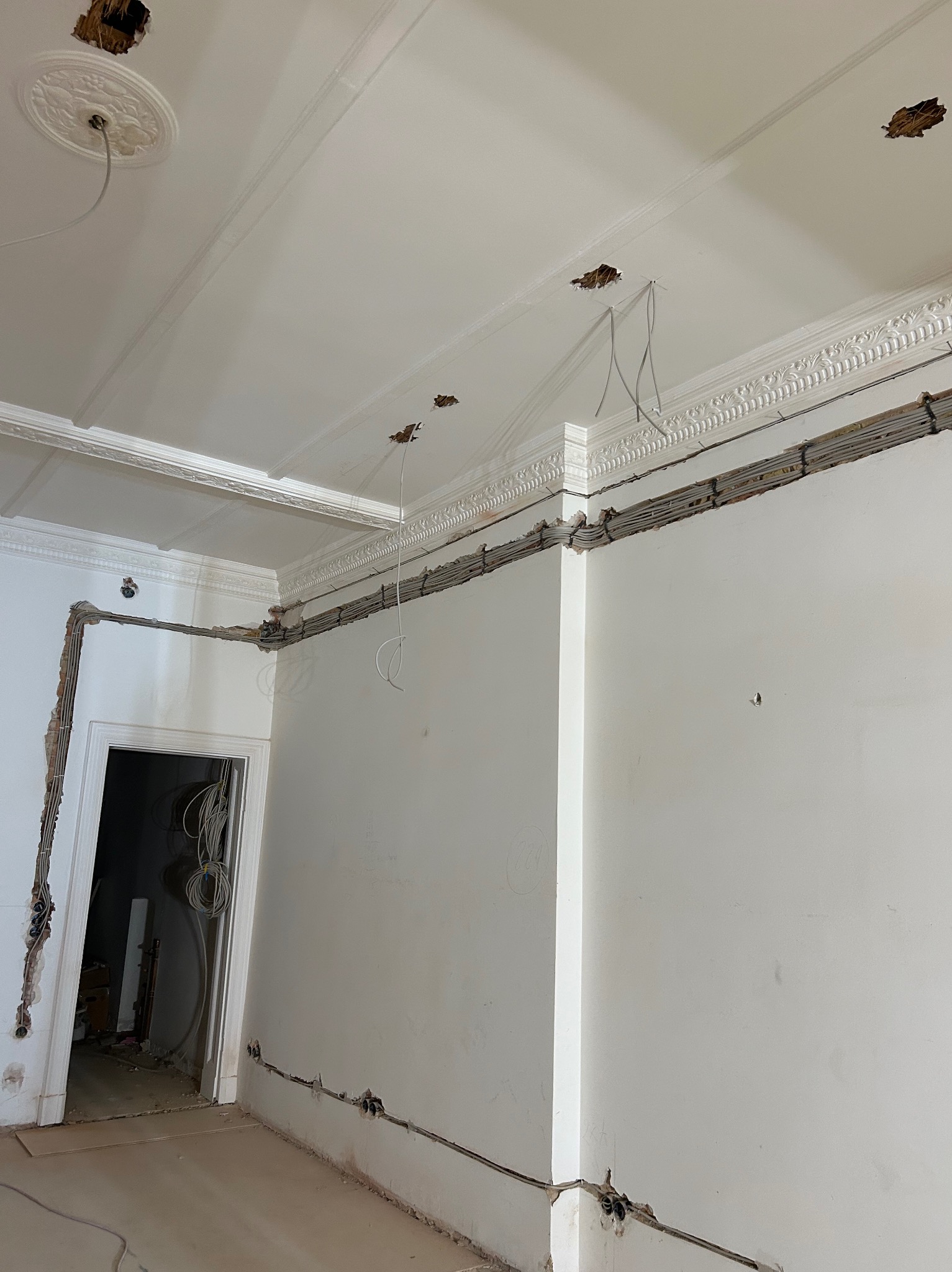 Wnętrze w trakcie remontu: widoczne kable elektryczne w ścianach i suficie, przygotowane otwory na oświetlenie. Dekoracyjne listwy sufitowe.