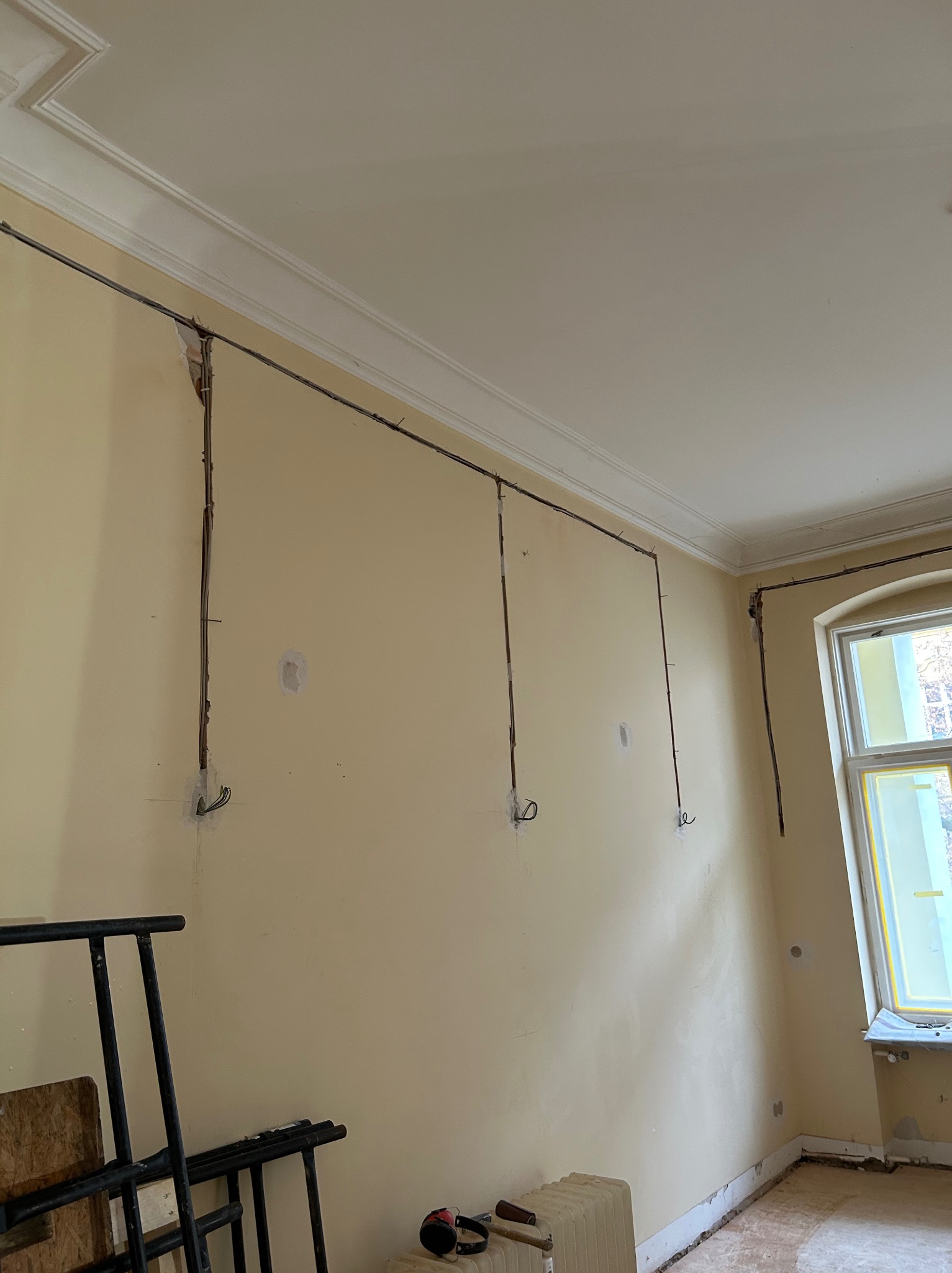Wnętrze w trakcie remontu: ściana z widocznymi przewodami elektrycznymi, przygotowanymi do instalacji. Przewody prowadzone natynkowo, widoczne puszki instalacyjne.