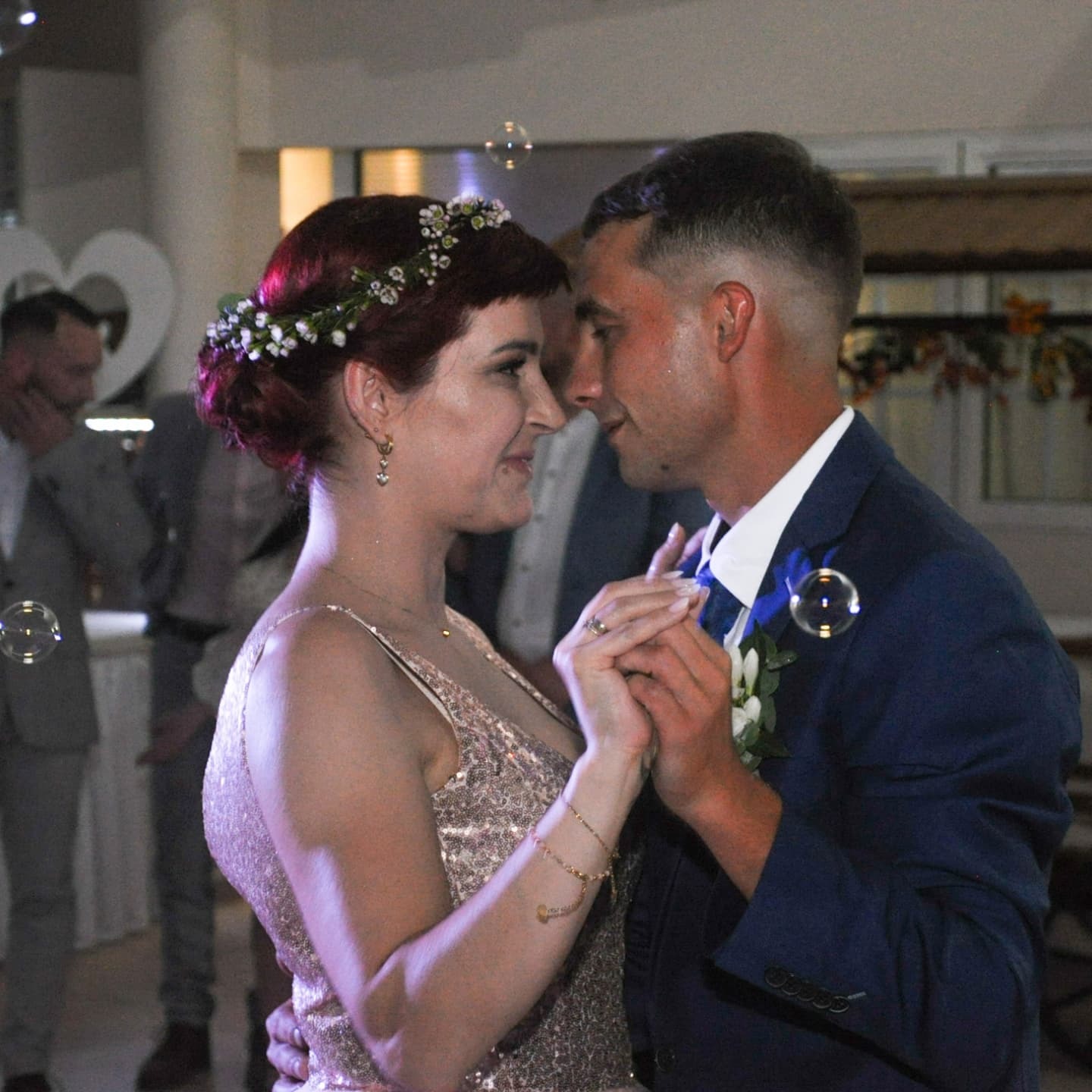 Para młoda w tańcu, panna młoda w cekinowej sukni i wianku, pan młody w granatowym garniturze, bańki mydlane w tle.