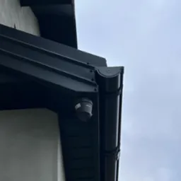 Kamera monitoringu Kenik zamontowana pod okapem dachu, obok rynny w kolorze grafitowym.