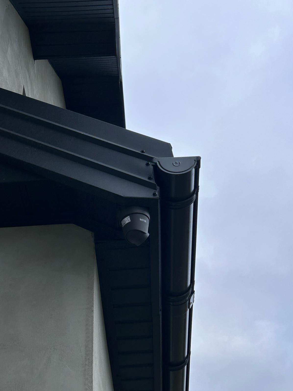 Kamera monitoringu Kenik zamontowana pod okapem dachu, obok rynny w kolorze grafitowym.