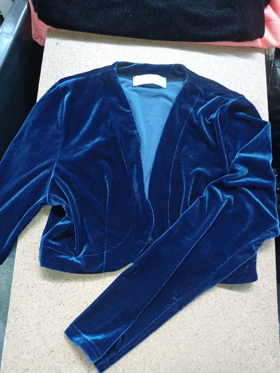 Krótki, granatowy, welurowy żakiet z długimi rękawami, leżący na jasnym tle.