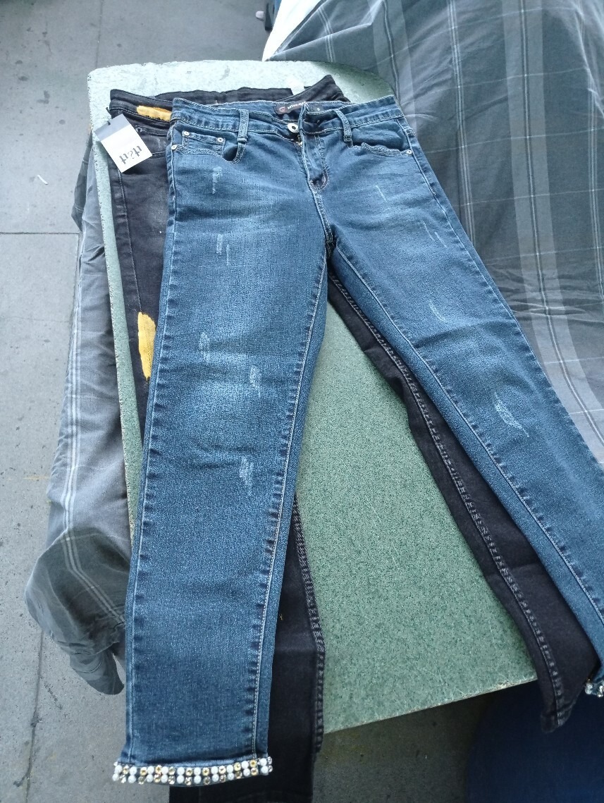 Stos spodni jeansowych, w tym niebieskie jeansy z ozdobnymi koralikami na dole nogawek, leżące na zielonym blacie