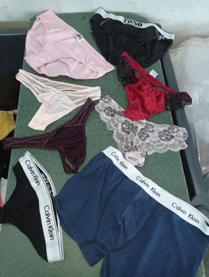 Różnorodny asortyment używanej bielizny damskiej i męskiej, z widocznymi markami Calvin Klein i Tono, ułożony na zielonej powierzchni, prezentujący różne style i materiały - od koronek po bawełnę.