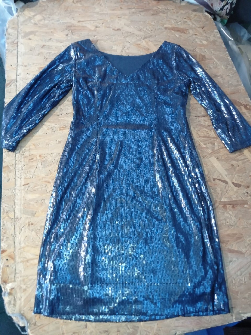 Błyszcząca, niebieska sukienka z długim rękawem, pokryta cekinami, leżąca na drewnianej powierzchni.