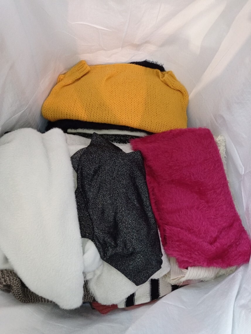 Stos ubrań w torbie, widoczne swetry w kolorach żółtym, białym, czarnym i różowym, różne faktury materiałów.