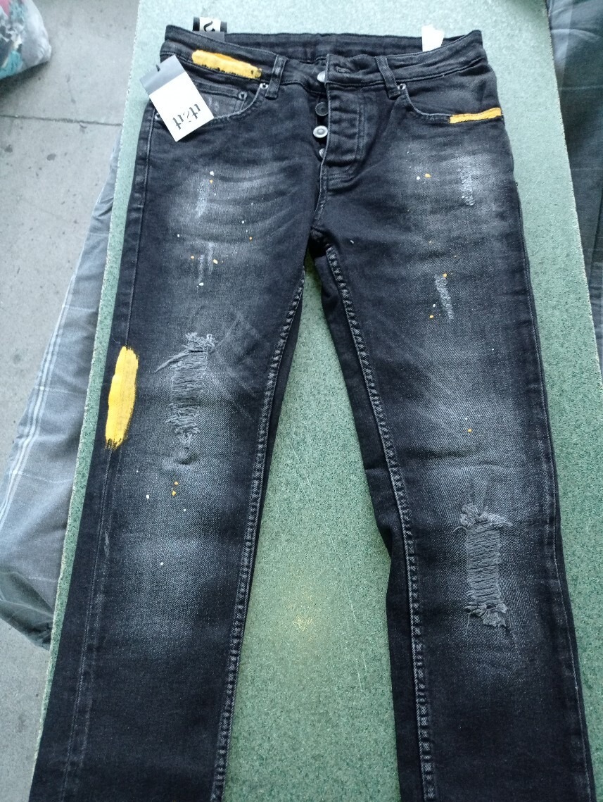 Czarne, używane jeansy typu slim fit z przetarciami, plamkami farby i żółtymi akcentami, leżące na zielonym tle, z widoczną metką.