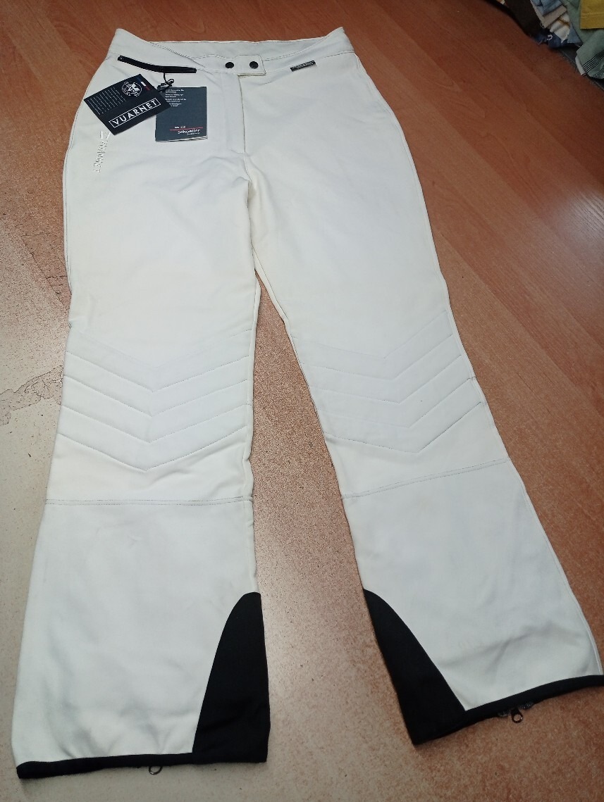 Jasne spodnie narciarskie marki Vuarnet z metkami, widoczne na drewnianej podłodze w Mierzynie, z czarnymi wstawkami na dole nogawek i charakterystycznym wzorem na kolanach.