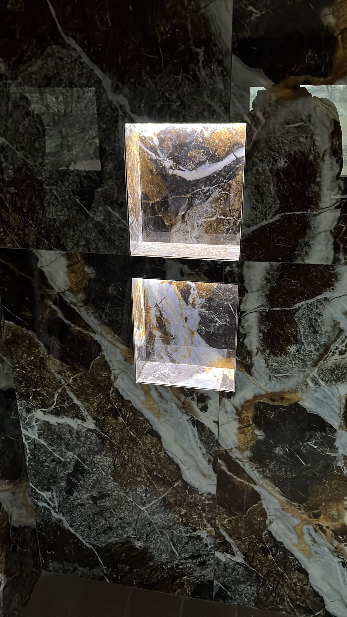 Wykończona ściana z ciemnego, żyłkowatego marmuru z dwoma wnękami oświetlonymi od góry, tworzącymi dekoracyjny element.