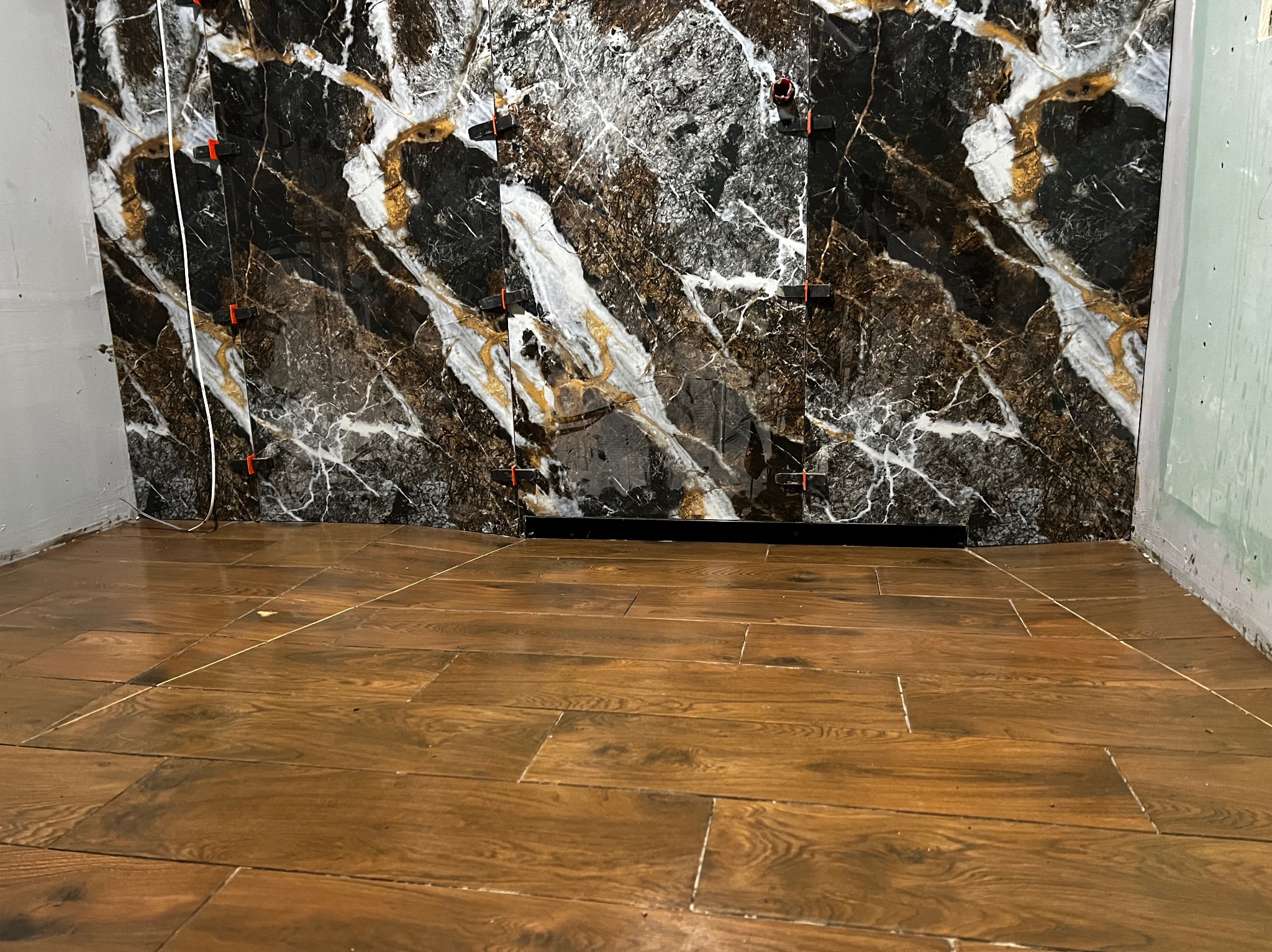 Montaż płytek imitujących marmur na ścianie, z użyciem klipsów poziomujących, oraz ułożona podłoga z płytek drewnopodobnych, widoczne fugi i nierówności podłoża.