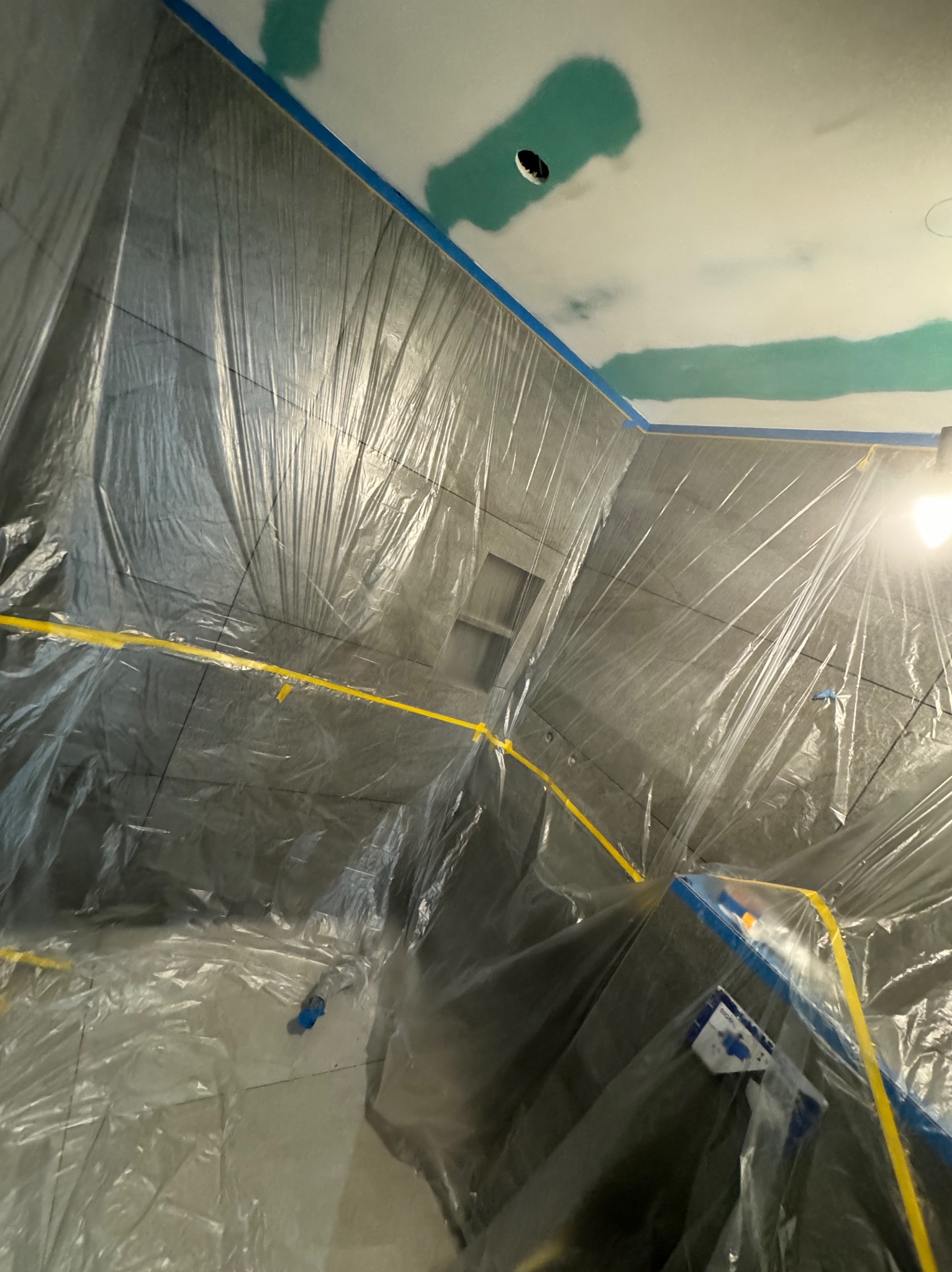 Łazienka w trakcie remontu, zabezpieczona folią malarską i taśmą, widoczne ślady gładzi na suficie.