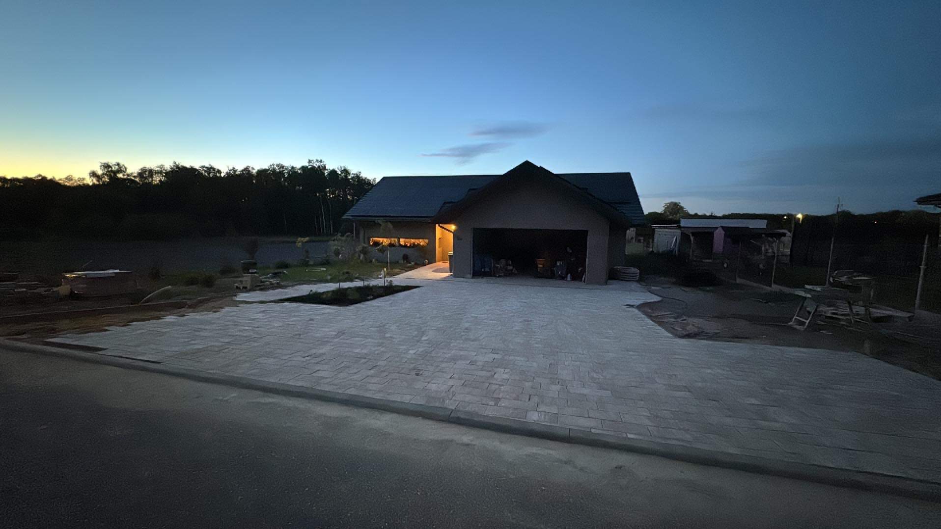 Nowoczesny dom jednorodzinny z garażem wbudowanym w bryłę budynku, podjazd wyłożony kostką brukową, widok o zmierzchu.