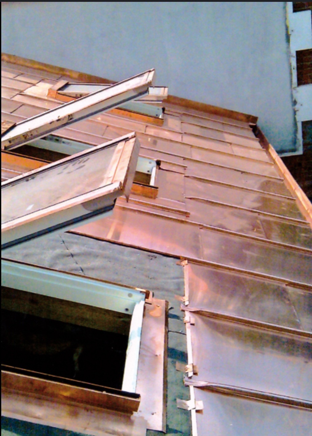 Miedziane poszycie dachu z oknami dachowymi w trakcie montażu, widoczne mocowania i warstwa izolacyjna, ujęcie z dołu.