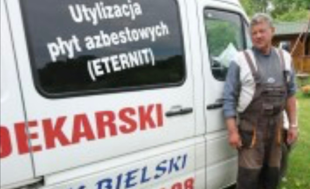 Dekarz w roboczym kombinezonie stoi obok białego samochodu z napisem 'Utylizacja płyt azbestowych (ETERNIT)' i dużym czerwonym napisem 'DEKARSKI' oraz nazwą firmy.