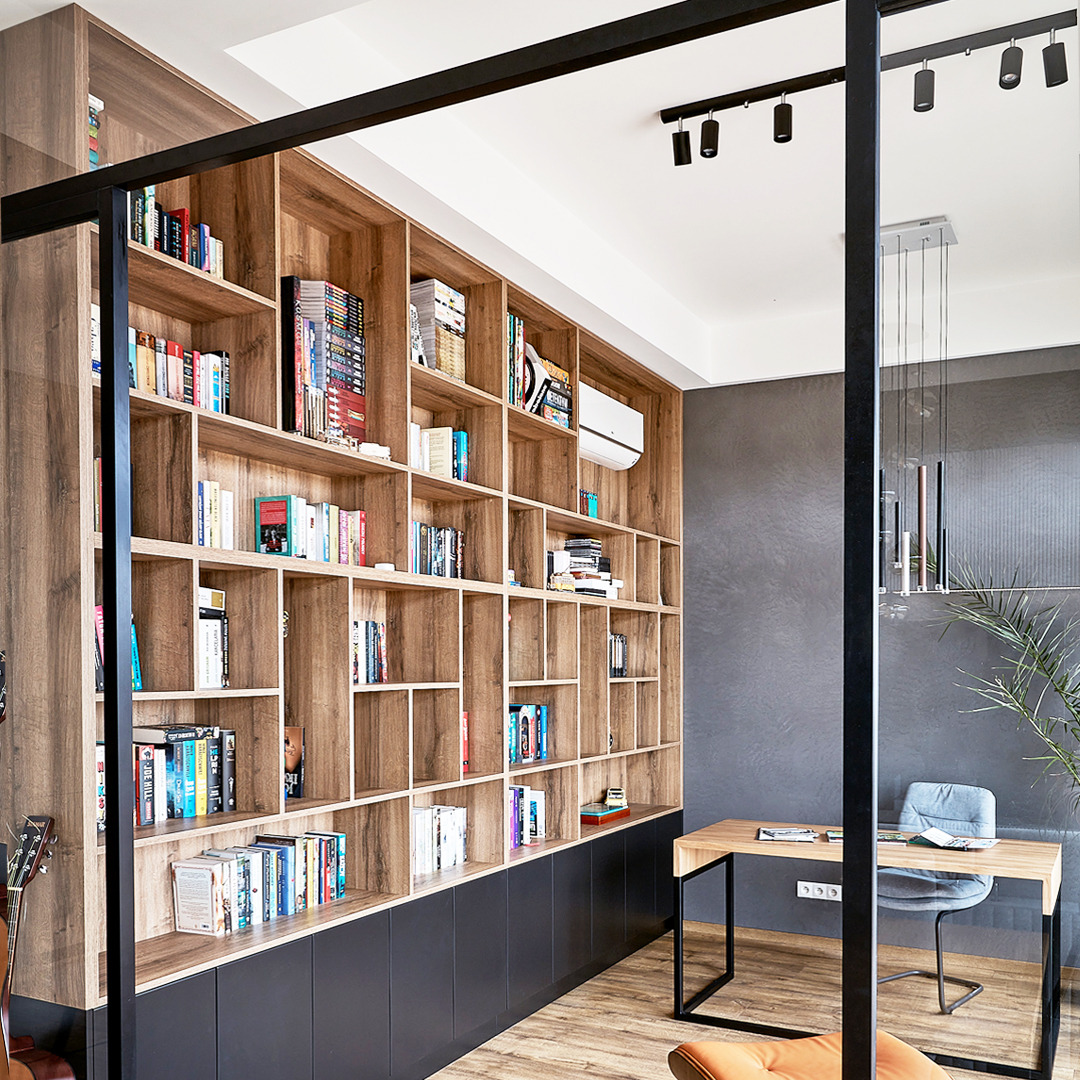 Drewniana zabudowa ściany z półkami na książki, połączona z szafkami w kolorze grafitowym, biurko w stylu industrialnym i szara ściana w tle.