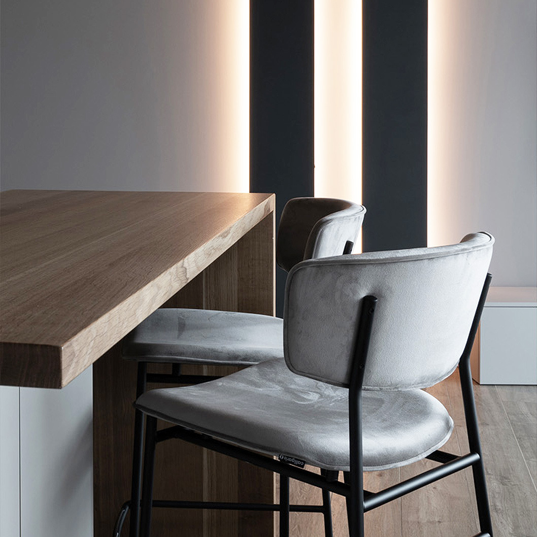 Detale nowoczesnej kuchni z drewnianym blatem i szarymi krzesłami barowymi na czarnych nogach, oświetlenie LED na ścianie.